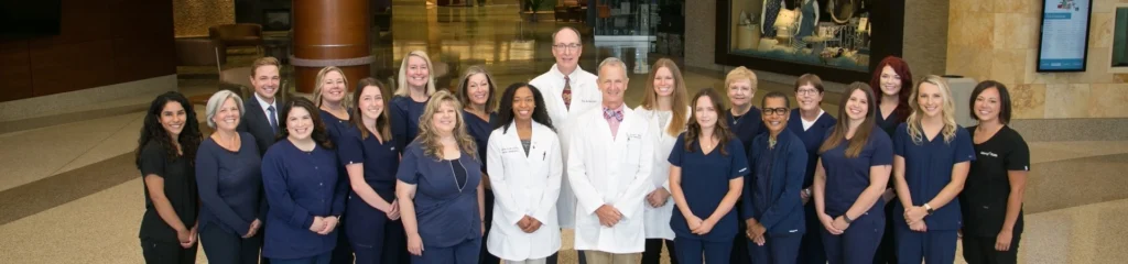 Dr. Waite and dental team members in white and dark uniforms posing together in modern office lobby.
