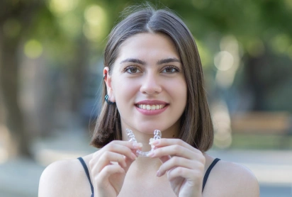 "Smiling woman holding Invisalign clear aligner, St. Louis, MO