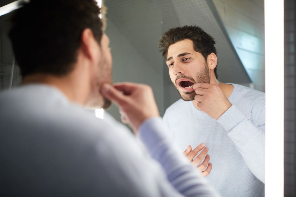 Man examining teeth in bathroom mirror for food debris or decay issues.