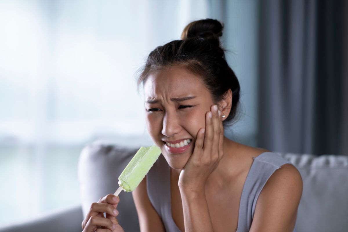 Woman experiencing tooth sensitivity pain while eating cold food.
